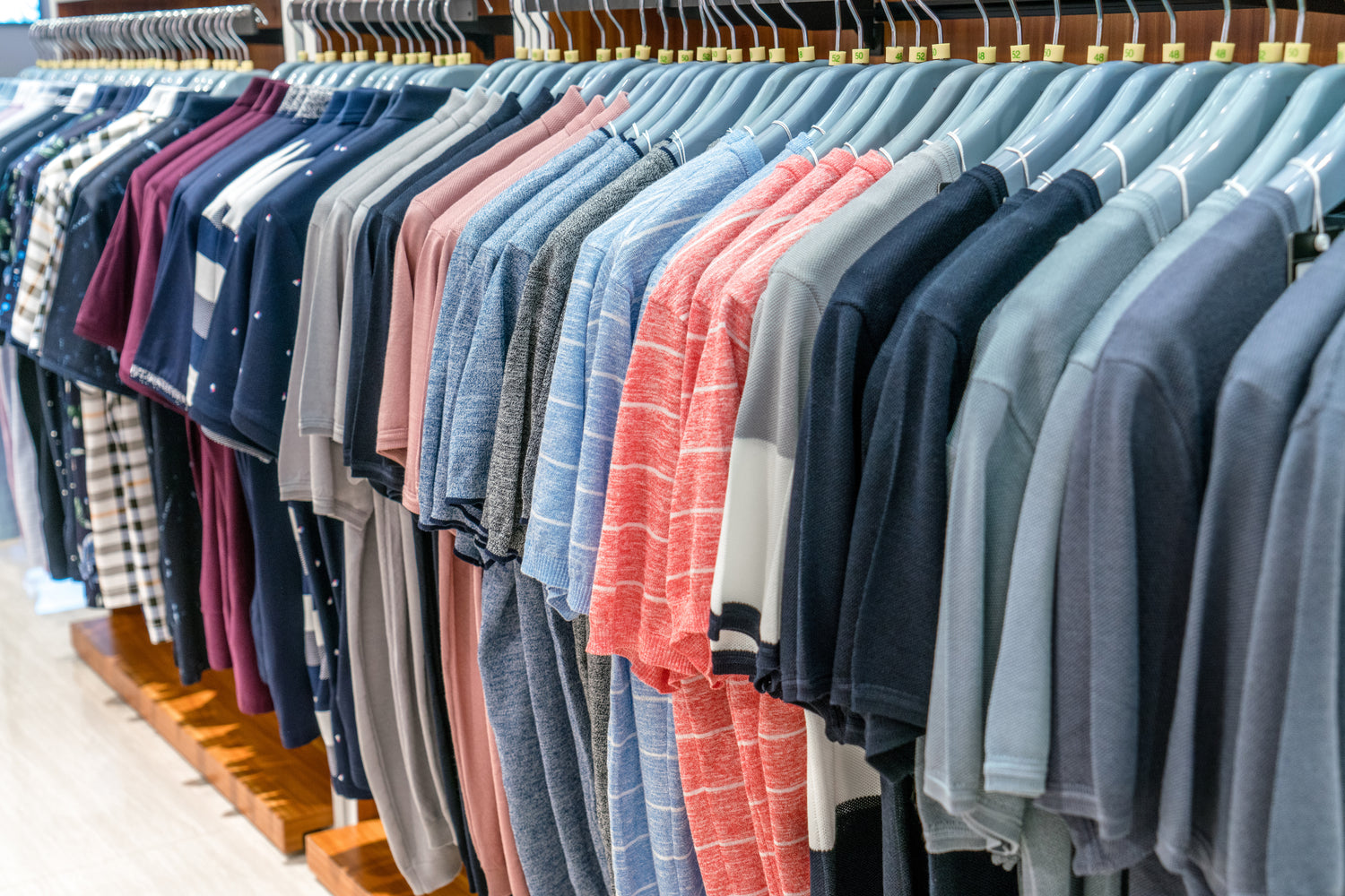 Rows of mass-produced shirts hanging on a rack, symbolizing the endless waste of fast fashion and overconsumption, contrasting with Clay & Ash’s focus on intentional, sustainable apparel